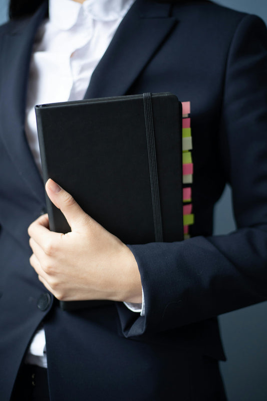 Woman in a navy blazer holding a tabbed black notebook, prepared to present a small claims court case