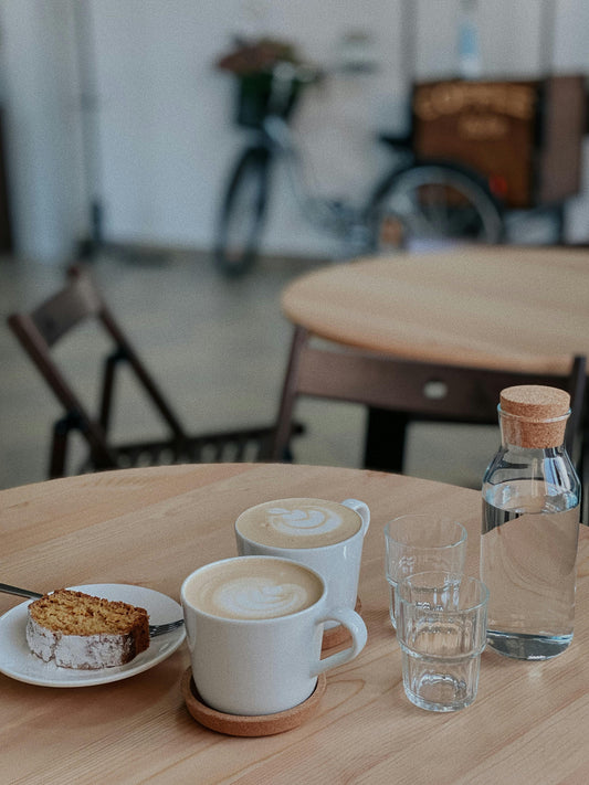 Two lattes, a slice of cake, and a water carafe on a cafe table, illustrating shared expenses between roommates