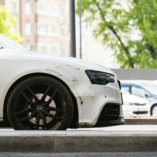 White car with a scraped front bumper and damaged paint parked at a curb, the kind of damage you can sue for in small