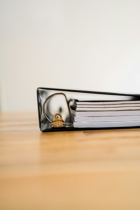 Black three-ring binder full of organized paperwork on a wooden desk, the kind of evidence judges look for in small claims